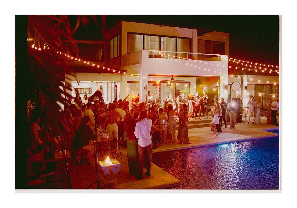 Film photograph of an evening reception on a terrace beside a pool, lit in red and orange