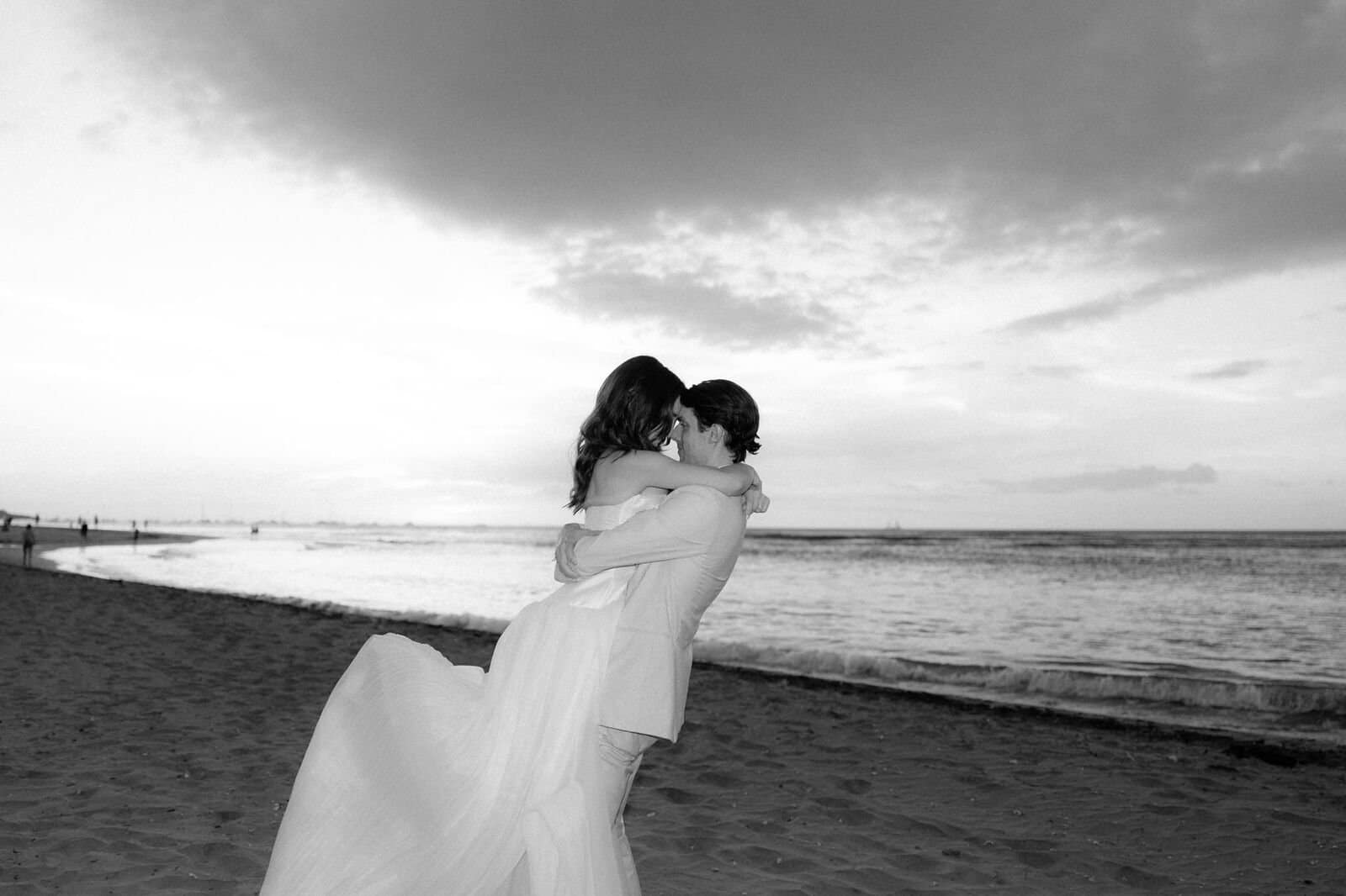 Black and white photo of a groom lifting his bride on the beach at sunset, Tamarindo, Costa Rica