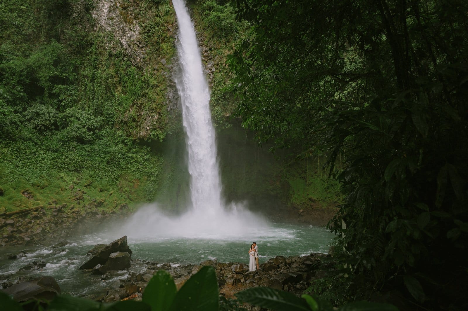 Tall rainforest waterfall with a tiny figure at its base, Costa Rica