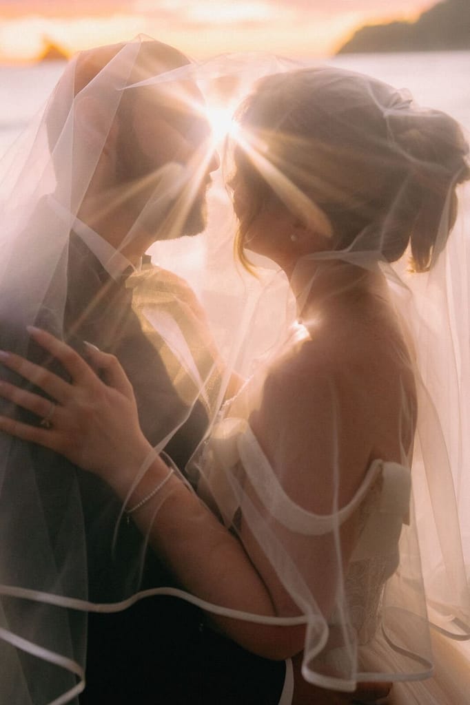 Bride and groom kissing beneath a sunlit veil at sunset by the ocean, Costa Rica