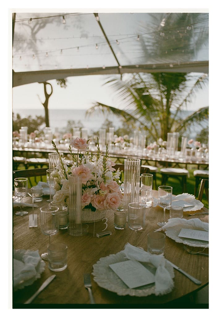 Film photograph of long reception tables with flowers under a tent and the ocean beyond