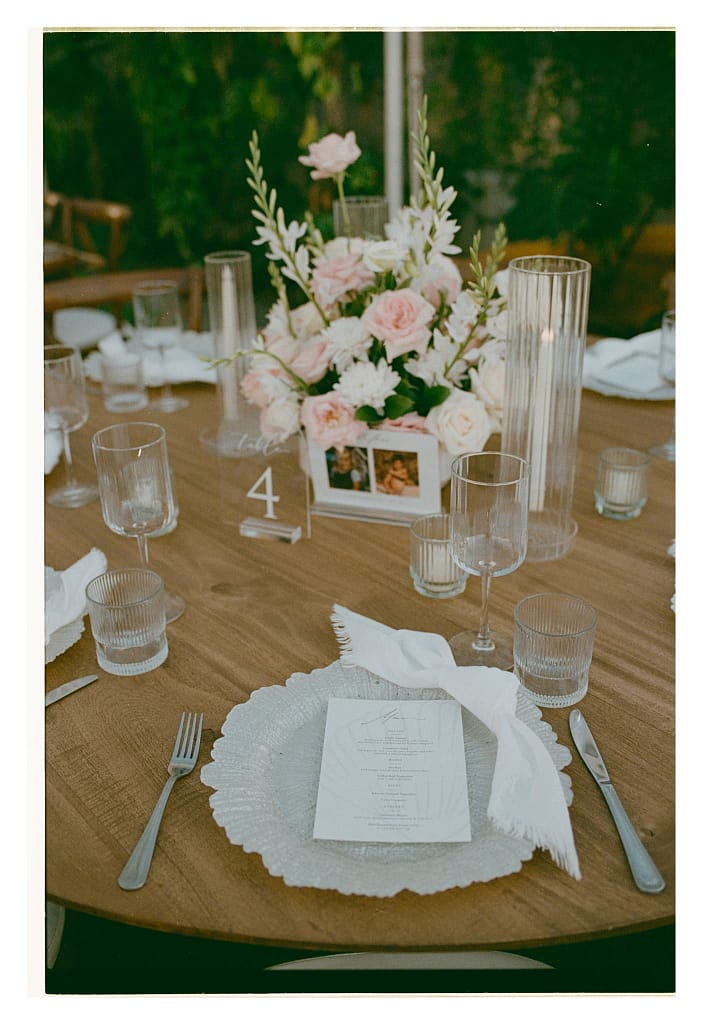 Film photograph of a round reception table with pink flowers, table number four and a printed menu