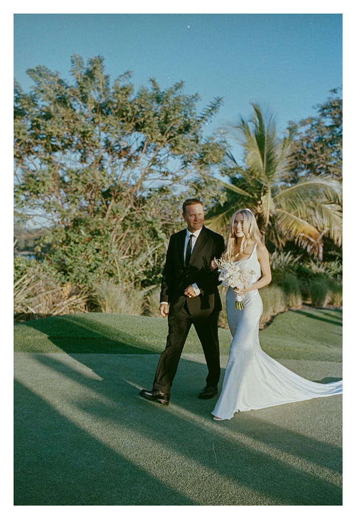 Film photograph of a bride in a white gown walking across the grass with a man in a dark suit