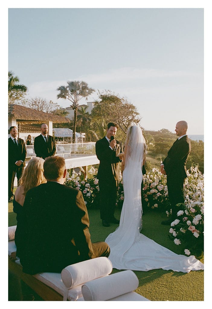Film photograph from behind the guests of a bride at the ceremony, surrounded by white flowers