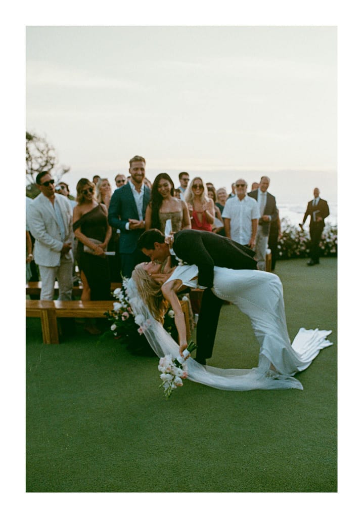 Film photograph of a couple’s ceremony kiss, the groom dipping the bride, with guests watching