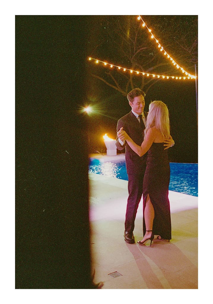 Film photograph of a couple dancing by a pool under string lights at night