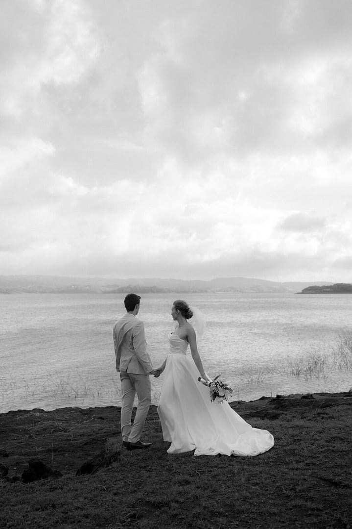 Black and white photo of a bride and groom holding hands on a rocky shoreline overlooking the bay, Costa Rica wedding