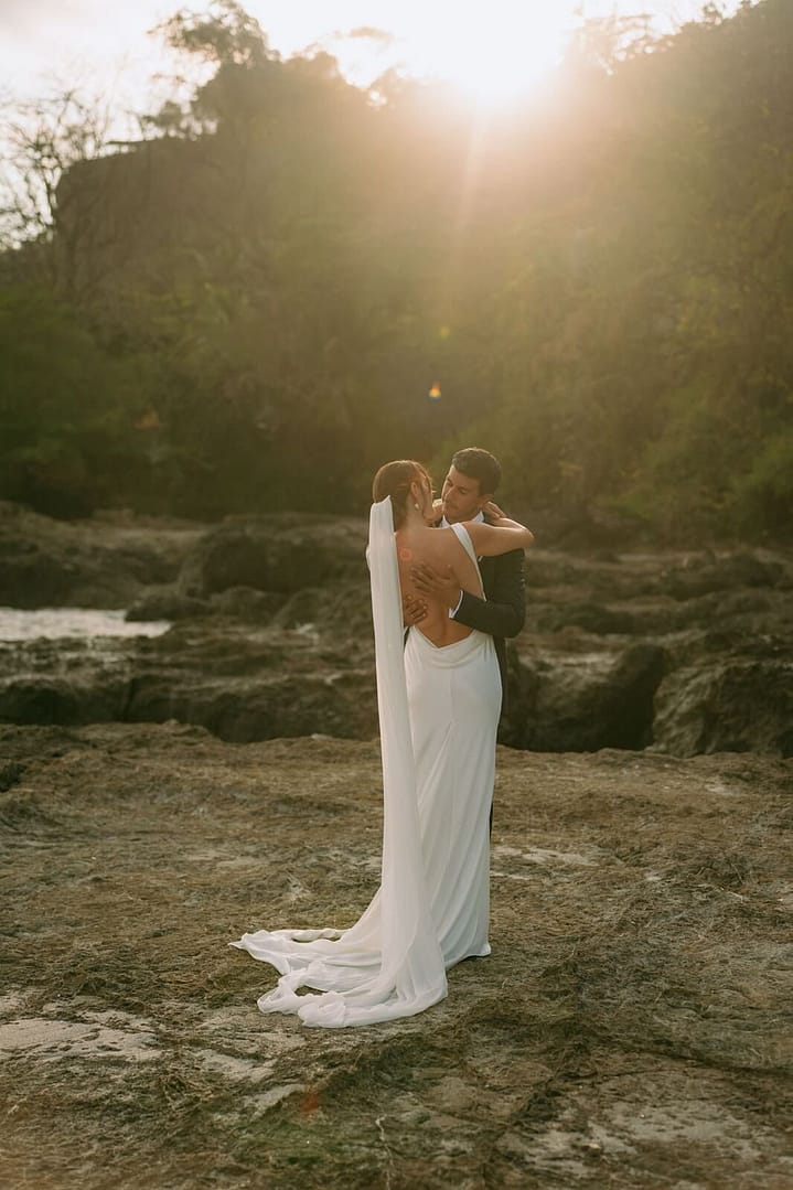 Bride and groom embracing on a rocky beach as the sun sets behind the headland, Costa Rica wedding