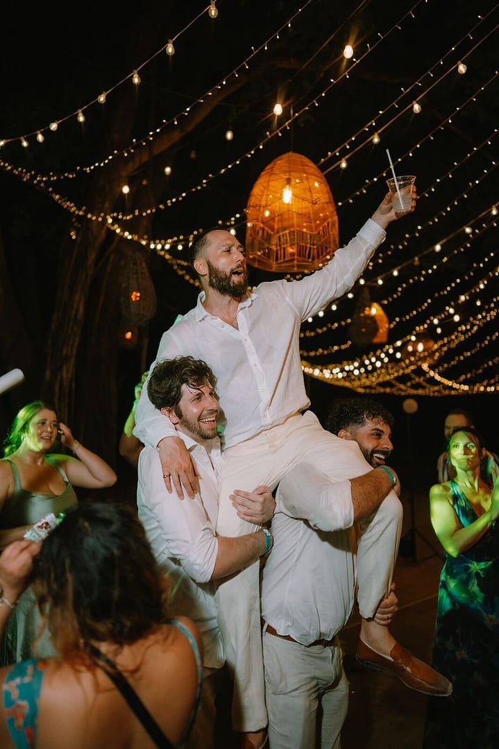 Wedding guests lifting the groom into the air on the dance floor under string lights, Costa Rica