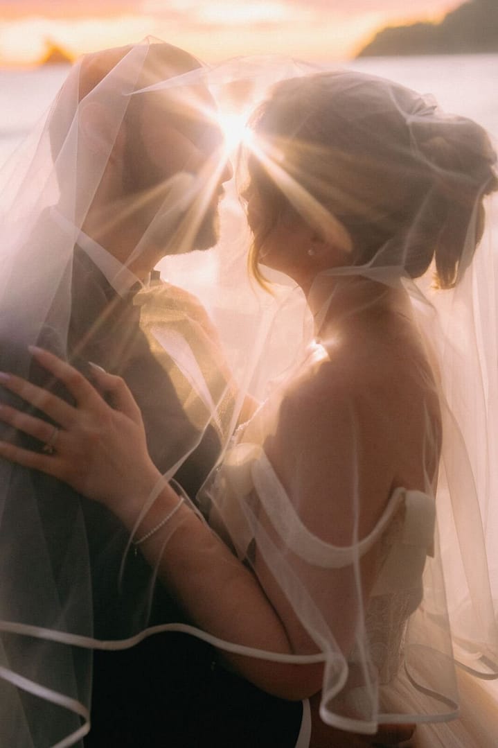 Bride and groom kissing beneath a sunlit veil at sunset by the ocean, Costa Rica
