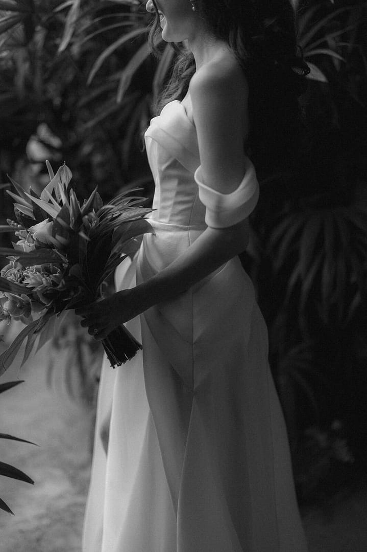 Black and white portrait of a bride holding a tropical bouquet among palm leaves, La Fortuna elopement, Costa Rica