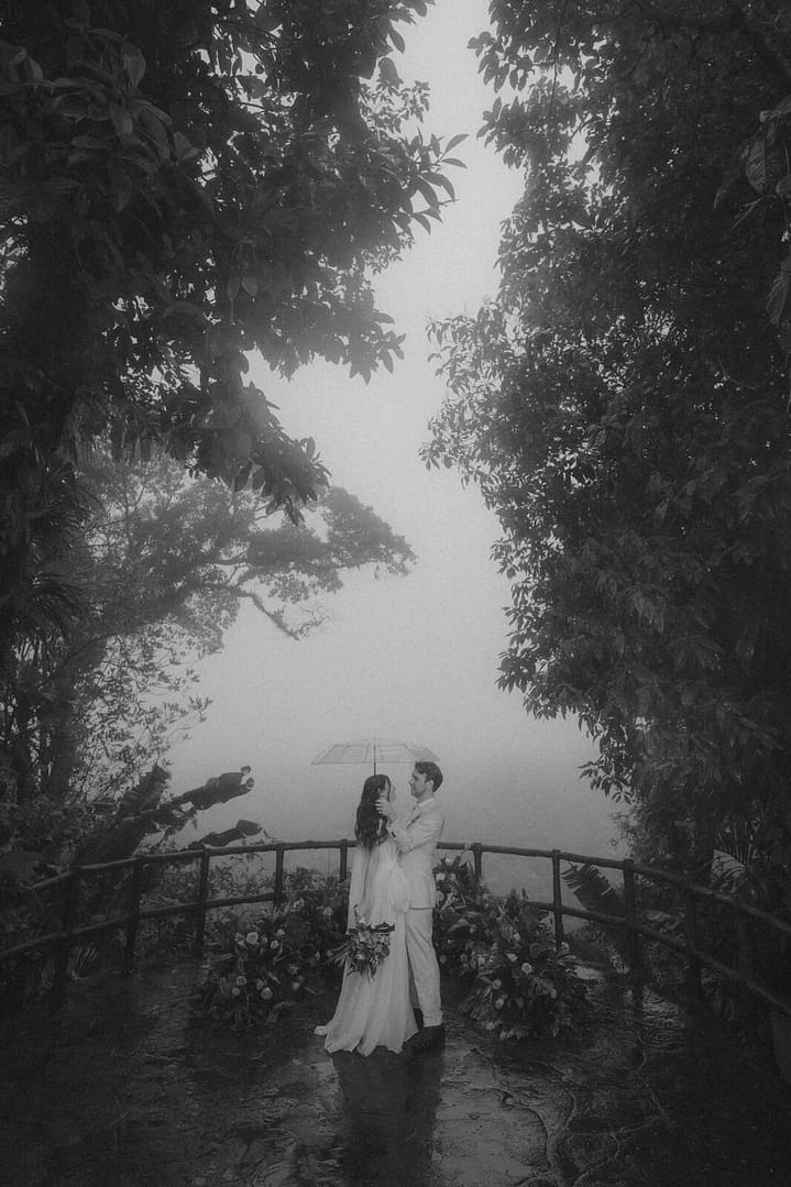 Couple embracing under an umbrella at a misty rainforest viewpoint during a La Fortuna elopement, Costa Rica