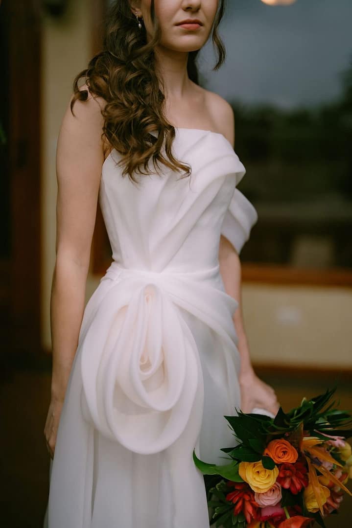 Bride in a sculpted white gown with a large rose detail holding a bright tropical bouquet, La Fortuna elopement, Costa Rica