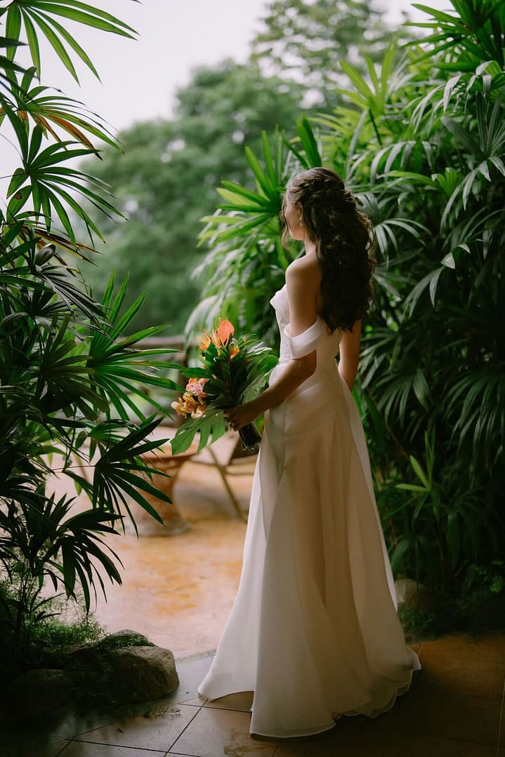 Bride in an off-the-shoulder gown standing among tropical palms during a La Fortuna elopement, Costa Rica