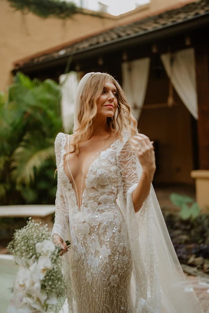 Bride in an ornate beaded gown and cape veil holding a white bouquet in a courtyard, Costa Rica wedding