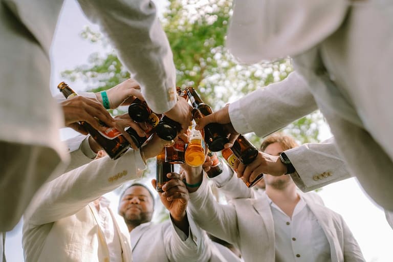 Groomsmen toasting with beers in a circle, photographed from below, at a Costa Rica wedding